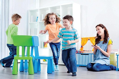 Toddlers playing an indoor game of musical chairs while a mom watches.