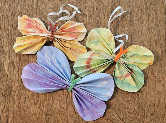 Three vibrant paper butterflies with ribbons resting on a wooden table surface.
