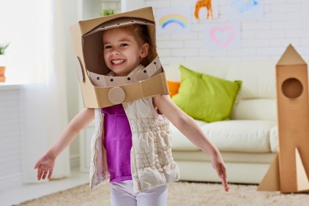 A preschooler playing make-believe, wearing a cardboard space helmet.