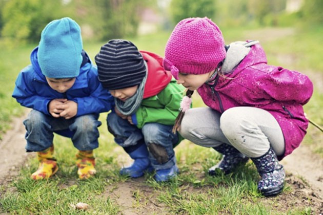 Kids wearing hats and jackets, crouching down to look at something in the grass.