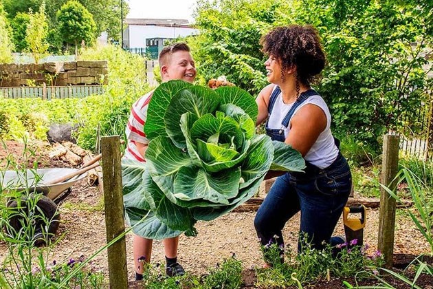 A child and an adult holding a giant cabbage in a community garden.