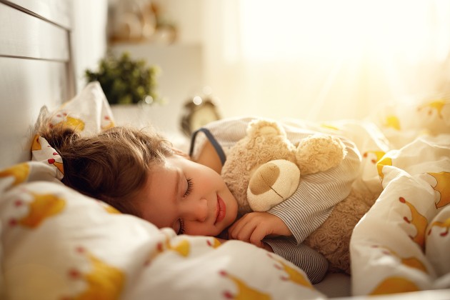 A toddler child sleeping and cuddling a plush toy bear.