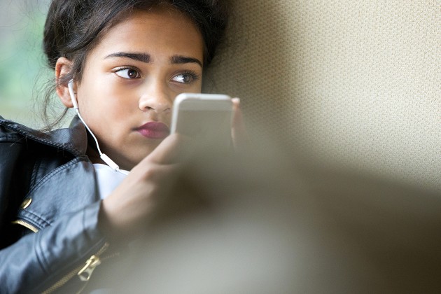 A teen wearing earbuds and holding an MP3 player.