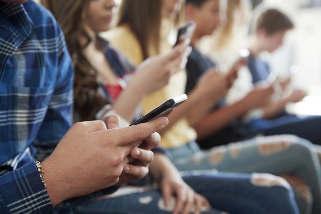 Grown-ups sitting in a row looking at cellphones. 