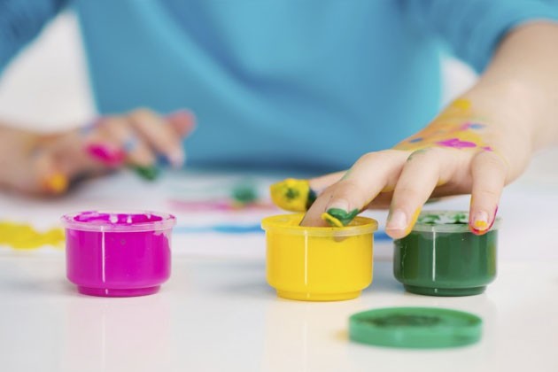 A child’s hand, dipping fingers into one of three small jars of paint