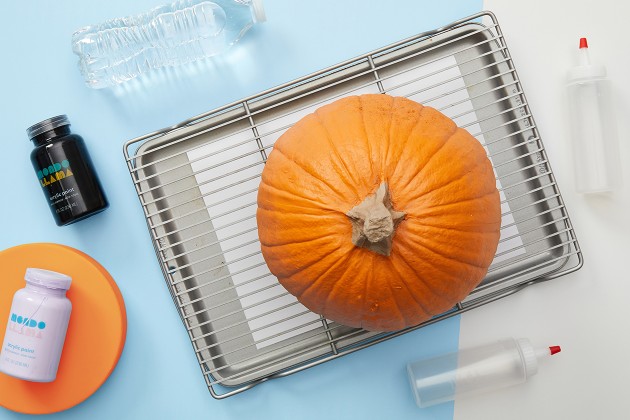 A pumpkin on a wire rack with a baking sheet under it.