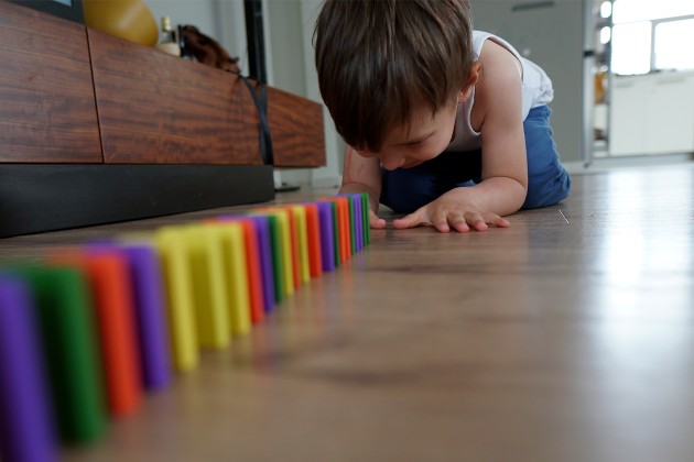 A child about to push the first domino in a row of multi-colored dominoes.