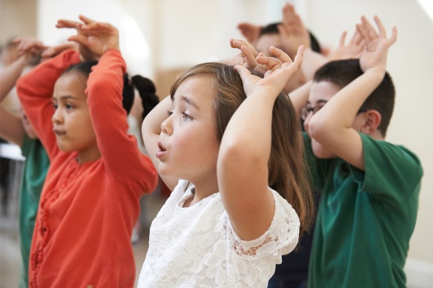 Kids singing while gesturing with their hands above their heads.