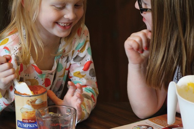 Two girls scooping pureed pumpkin out of a can.