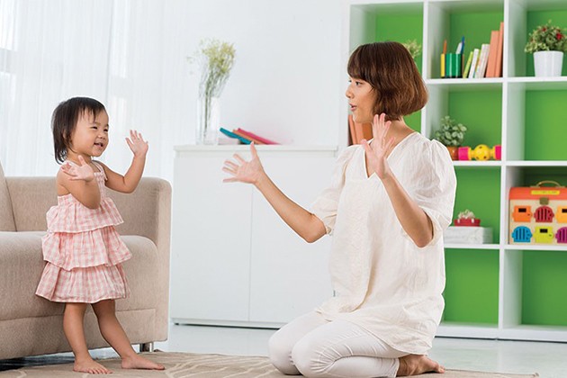 Mother and baby waving hands in the air while singing together.