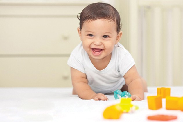 Smiling baby crawling on bed with play toys nearby