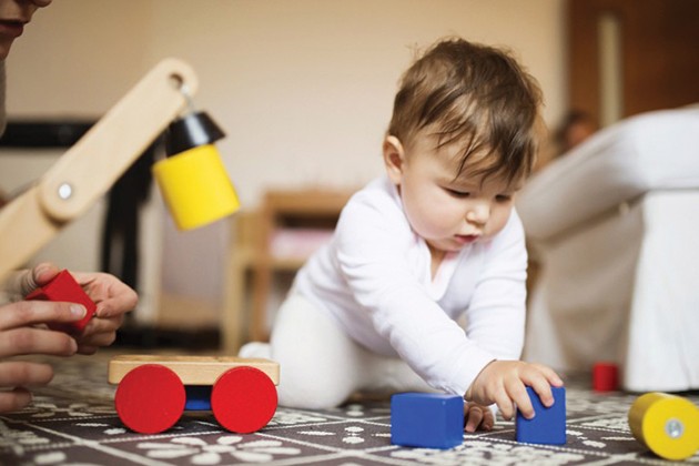 Baby playing on a rug with blocks and pull toys.