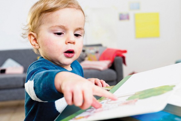 Toddler pointing to story book on coffee table.