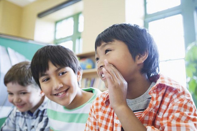 Three boys whispering secrets to each other in a classroom.