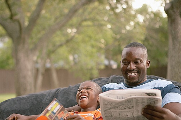 Man and young boy reading books together outside.