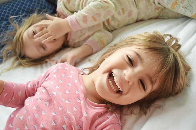 Two preschool-age girls in pajamas laughing on a bed.