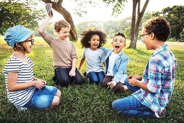Five children sitting under trees, laughing together.