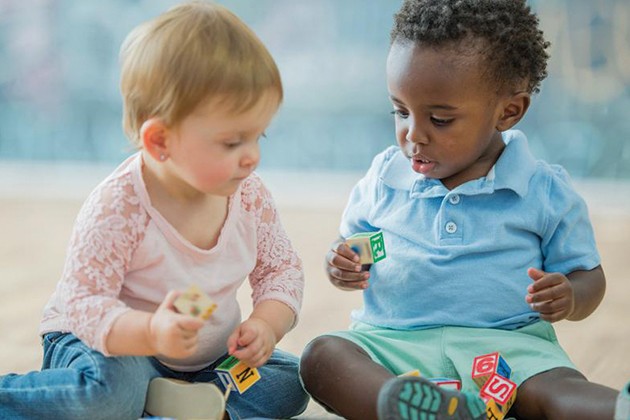 Two babies playing with blocks next to each other.