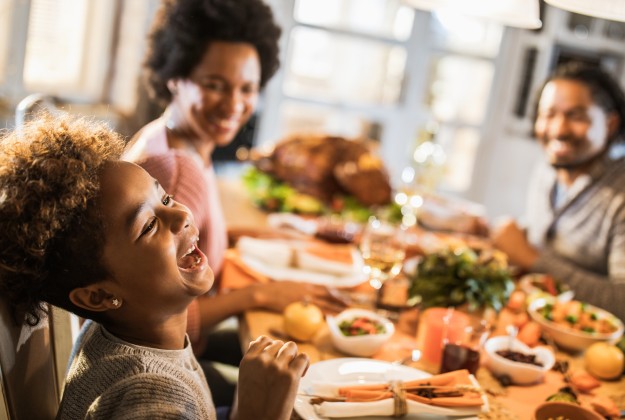 Family laughing and telling jokes around the Thanksgiving dinner table.