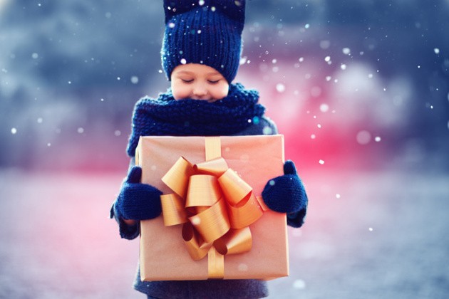Little boy holding a gift with gold wrapping paper in the snow.