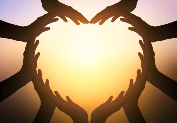 A group of helper hands joined to form a heart with a sunset in the background.