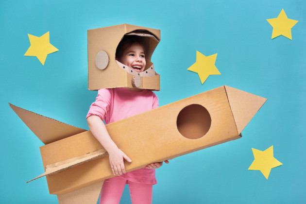 Little girl wearing a pink sweatshirt and holding a space rocket made out of cardboard.