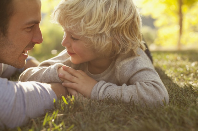 Little boy and dad smiling at each other while lying in grass.