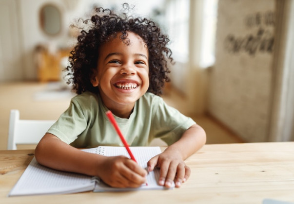 Little boy sitting at a desk and smiling with a pencil and paper 