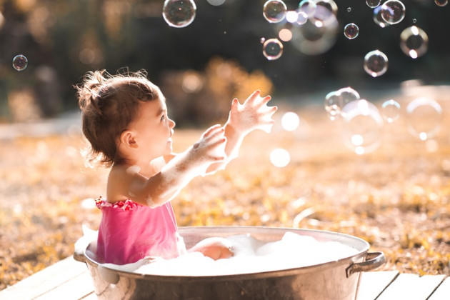 Laughing baby girl playing with soap bubbles outdoors.