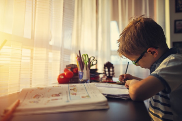 Young boy sitting at a desk doing homework by a window.