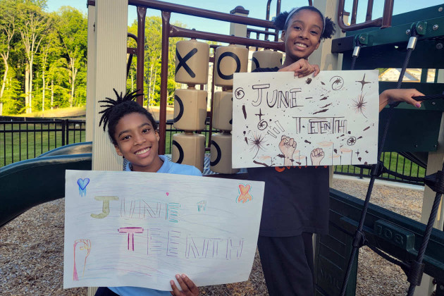 Two teen Black girls hold colorful signs that say Juneteenth on them.