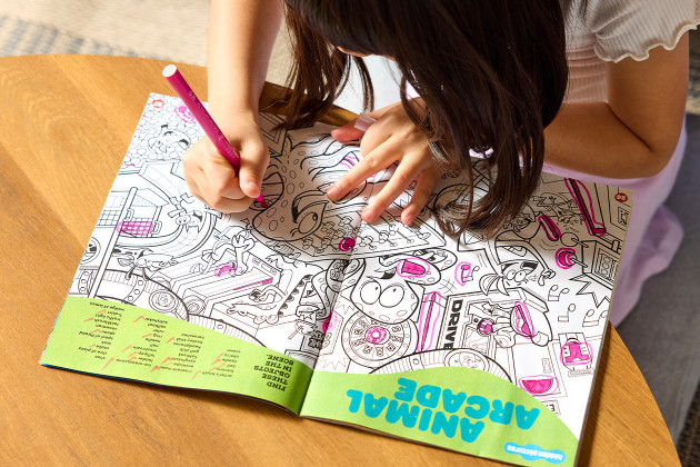 A young child using a bright pink marker to seek and find the hidden objects in her Highlights Hidden Pictures puzzle book