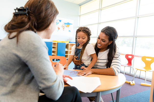 parent with child talking with teacher at parent-teacher conference