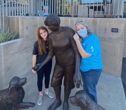 Ariela and an adult pose by a bronze statue of a person and two dogs. 