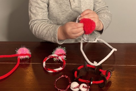 A child using chenille stems and pompom balls to make jewelry.