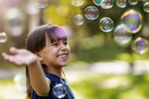 A child swatting at soap bubbles outdoors.