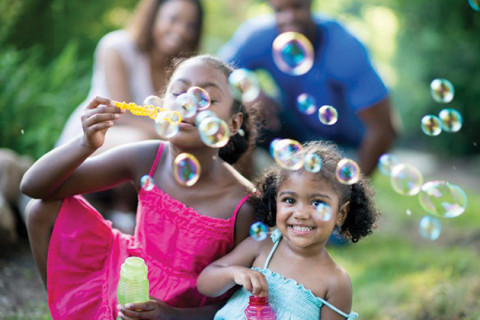 Two girls in sundresses blowing bubbles outside. 