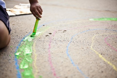 A child painting with homemade sidewalk paint on the pavement.