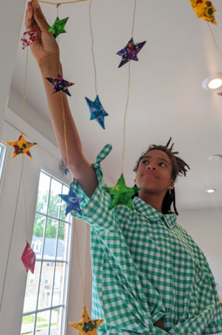 A smiling girl hangs colorful stars to celebrate Juneteenth.