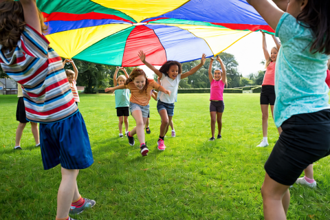 group of kids in lawn playing outdoors with big rainbow parachute